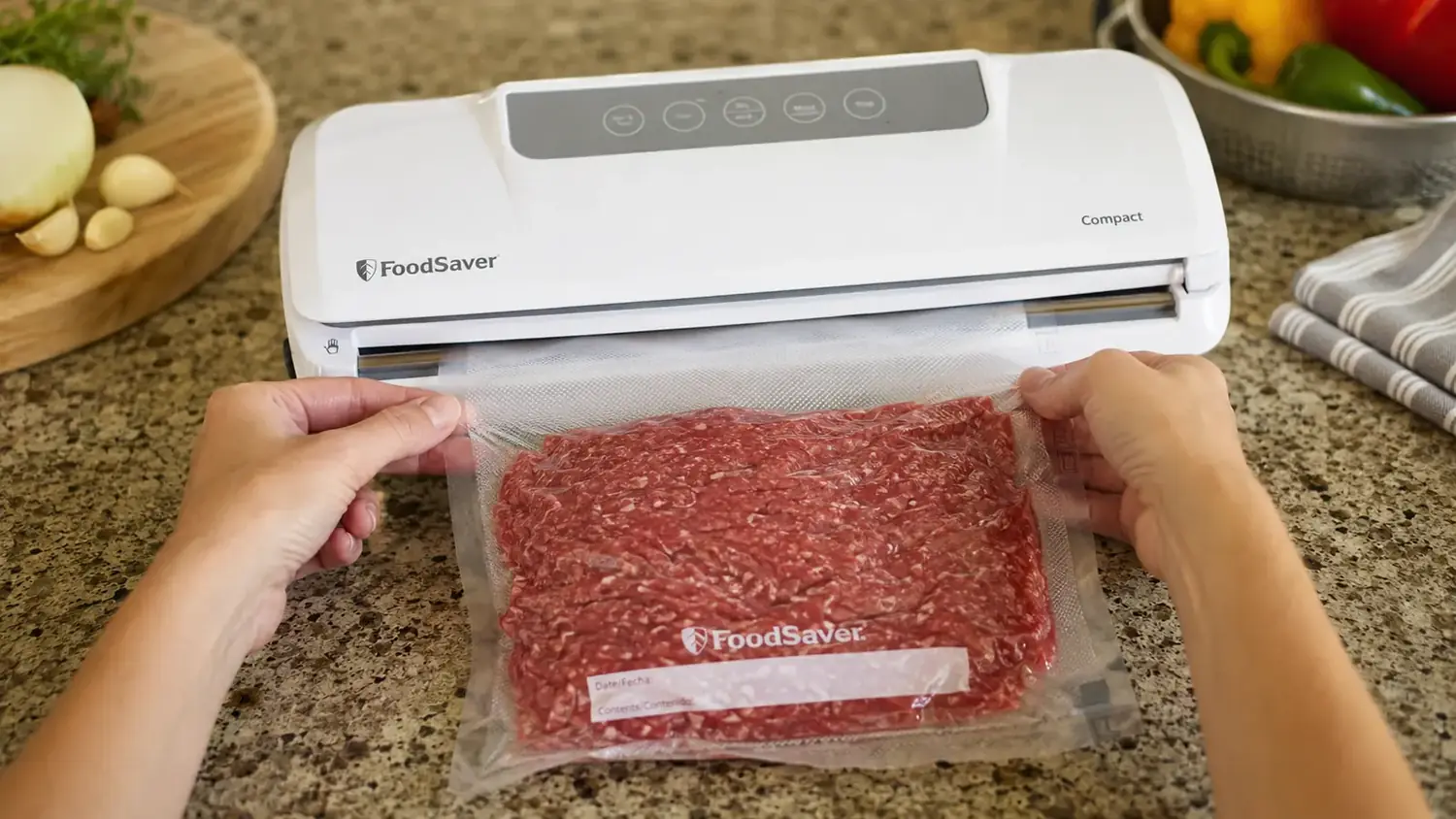 Close-up of hands guiding a bag of ground beef into a countertop vacuum sealer