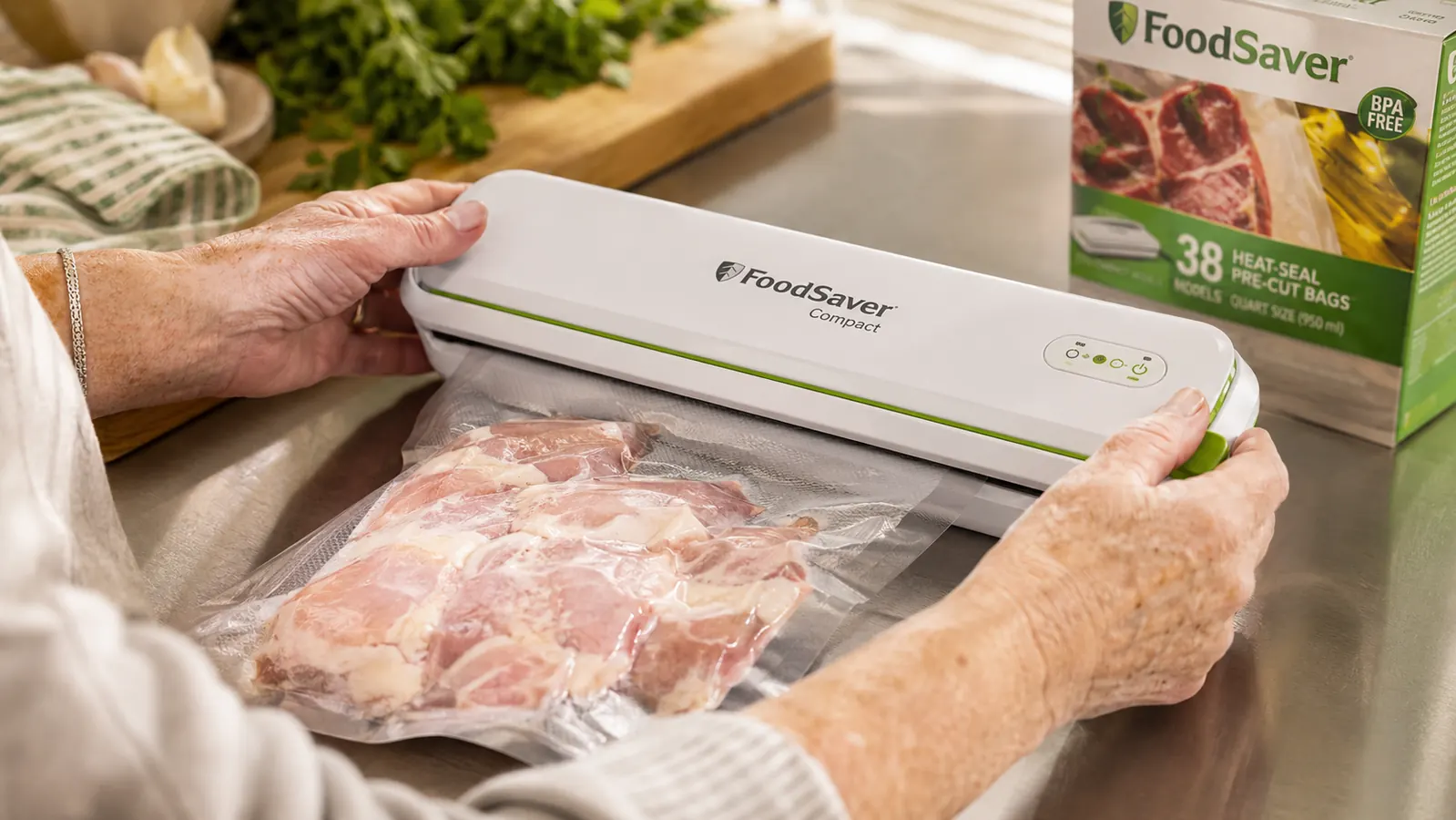 Hands sealing a bag of raw chicken thighs in the FoodSaver Compact vacuum sealer on a stainless counter