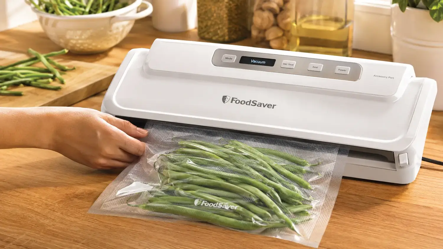 Hand feeding a bag of garden green beans into the FoodSaver Compact Vacuum Sealer as the machine pulls the air out and seals the edge