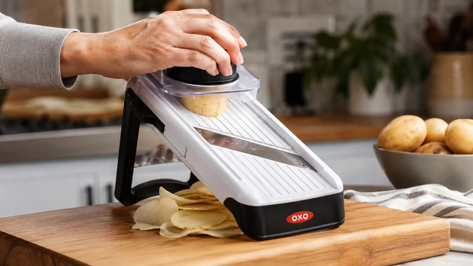 A hand guiding a potato through the OXO mandoline slicer with the hand guard attached