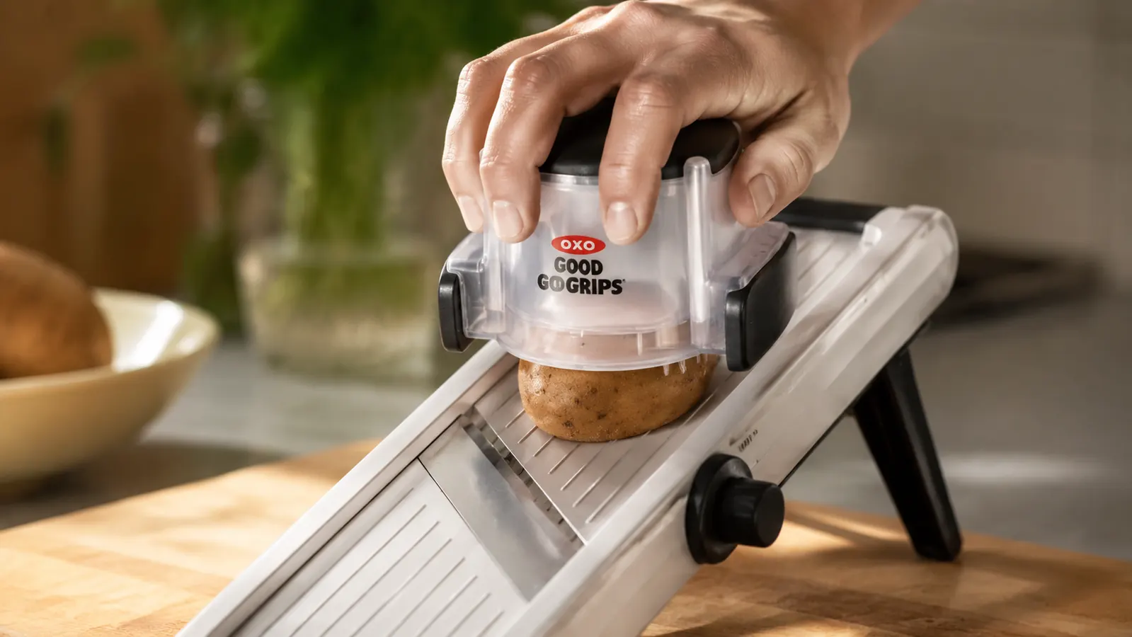 Hand using the food holder attachment to guide a potato across the OXO mandoline blade