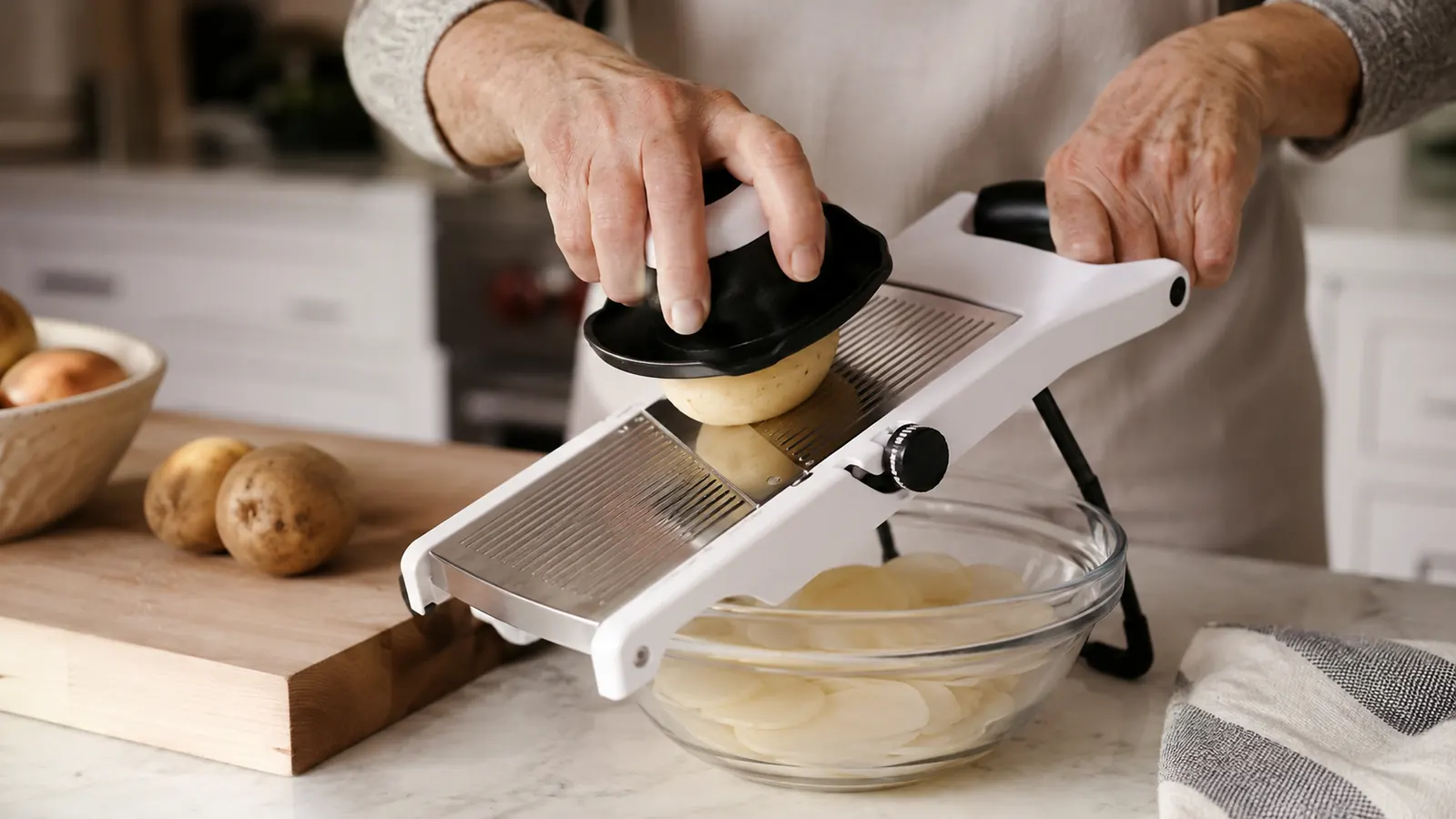 Hand using the OXO Good Grips mandoline slicer with the food holder to slice a potato into even rounds over a bowl