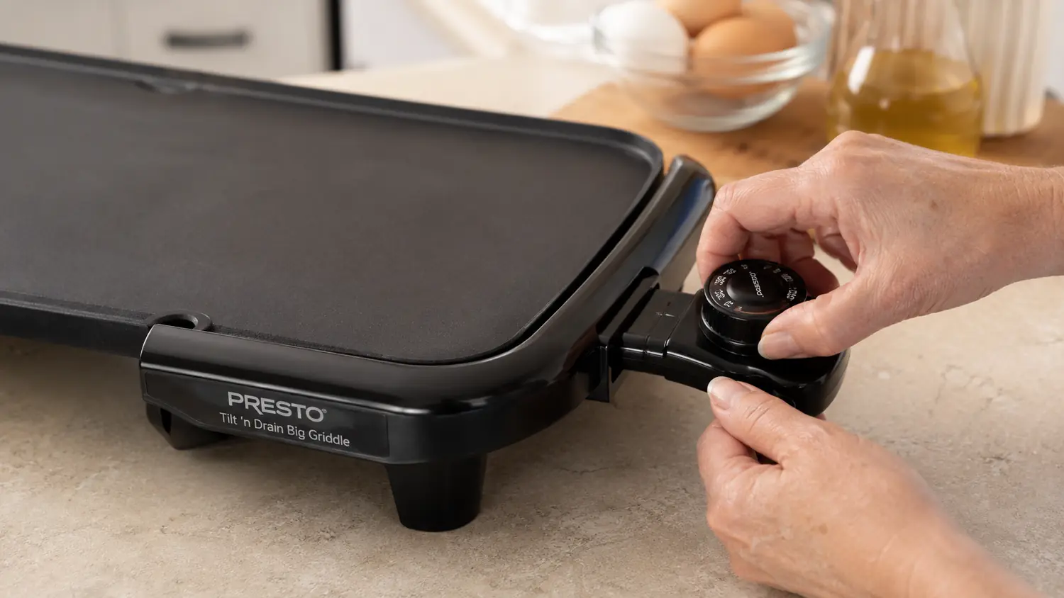 Close-up of a hand adjusting the temperature dial on the Presto griddle's control knob