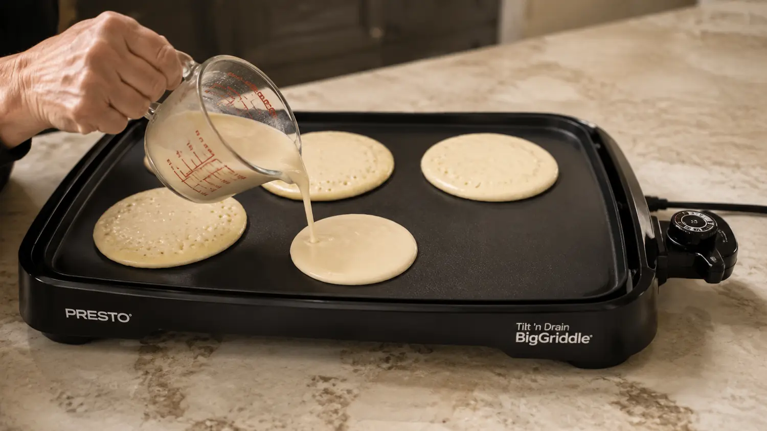 Hand pouring pancake batter onto the Presto griddle's nonstick surface next to the temperature dial